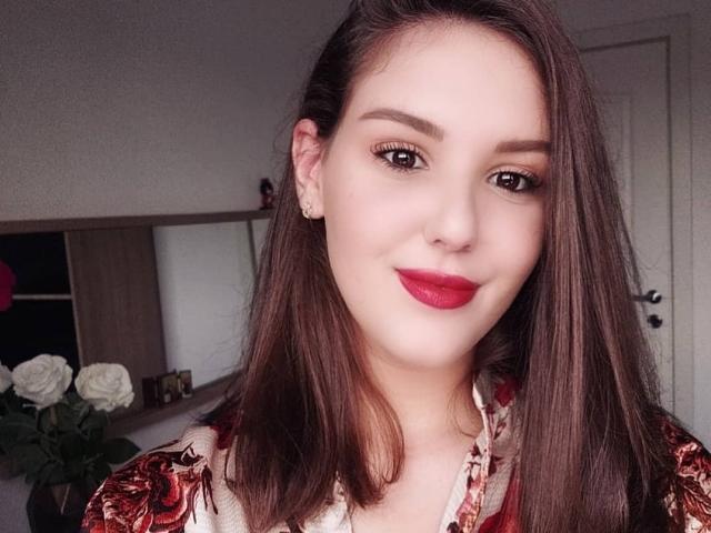 ChristineRayssa has medium-length brown hair, red lipstick, and is wearing a floral shirt. She's smiling with her eyes looking slightly to the side. Her tits are not visible.