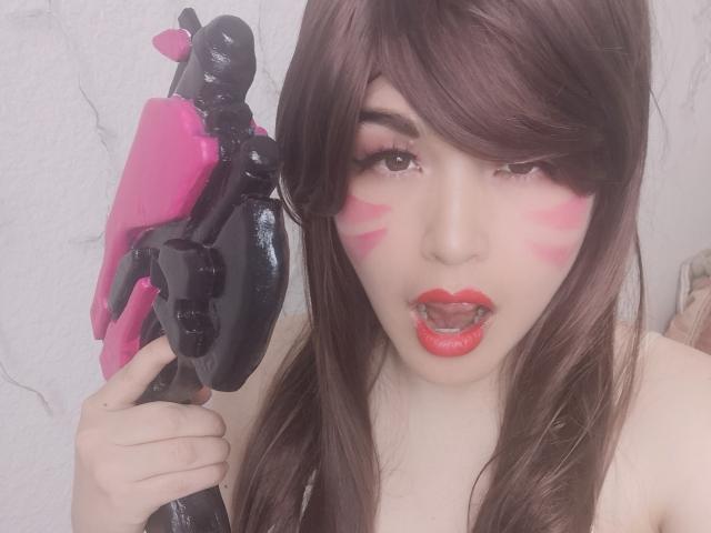 HikaruChan con maquillaje rosa en la cara, lápiz labial rojo y cabello castaño, sosteniendo una pistola de agua negra y rosa, con la lengua afuera, luciendo sexy, con piel pálida y una expresión linda..