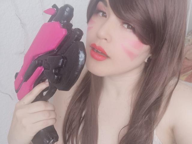 HikaruChan con maquillaje rosa en la cara, lápiz labial rojo y cabello castaño, sosteniendo una pistola de agua negra y rosa, mirando a la cámara con la boca ligeramente abierta..