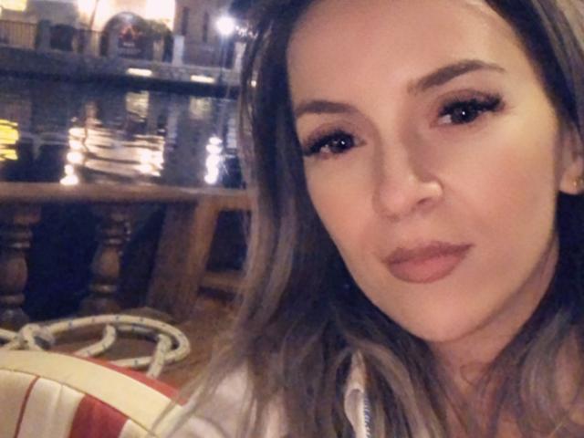 SophieDeee has long brown hair, thick eyebrows, and is wearing eyeliner with mascara. She's looking at the camera with a slight smile, her pink lips are slightly parted.