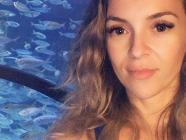 SophieDeee tiene el cabello rubio ondulado, piel clara y ojos marrones, con una ligera sonrisa. Sus pequeños senos apenas son visibles en la foto. Está bajo el agua..
