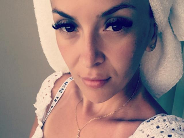 SophieDeee with a white towel on her head, wearing a crocheted top, showing off her long, thick, black eyelashes and a subtle, confident smile. Her tits are barely visible.