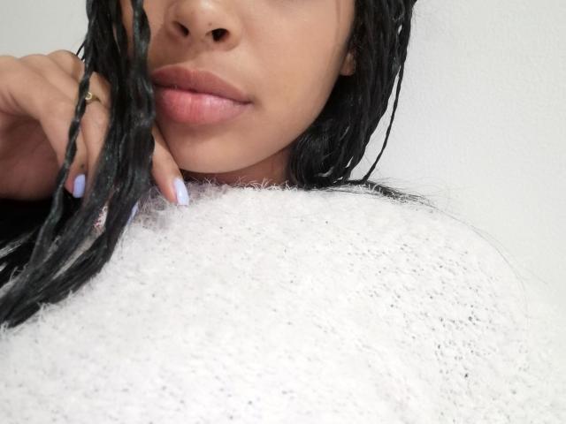 VickyGreys with wet black braids, full pink lips, and light brown skin, wearing a fluffy white bathrobe, showing her tits and a hand with pastel purple nails.