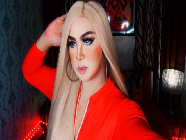 BornStarTS with long blonde hair, blue eyes, red eyeliner, and red top, hand in hair, looking at camera, red light on left, hoop earrings, makeup, and a sexy face.