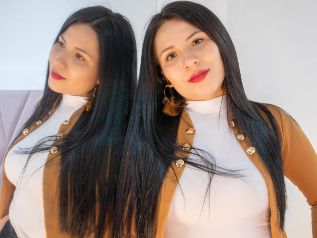 Bethany Roberts mit langem, schwarzem Haar, rotem Lippenstift, trägt einen weißen Rollkragenpullover und einen braunen Pullover mit goldenen Knöpfen und steht vor einem Spiegel und zeigt ihre Brüste..