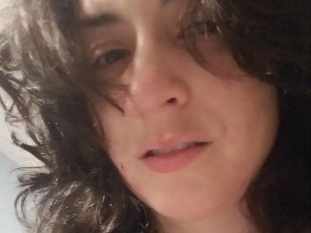 LiveSex with curly brown hair, slightly parted lips, and a small mole on the right cheek, showing a relaxed, slightly open-mouthed expression.