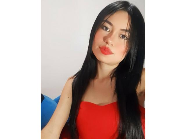 LolyFunX with long black hair, red lipstick, and a red strapless top, showing her tits slightly, has a cute, sexy face, and a subtle pout.