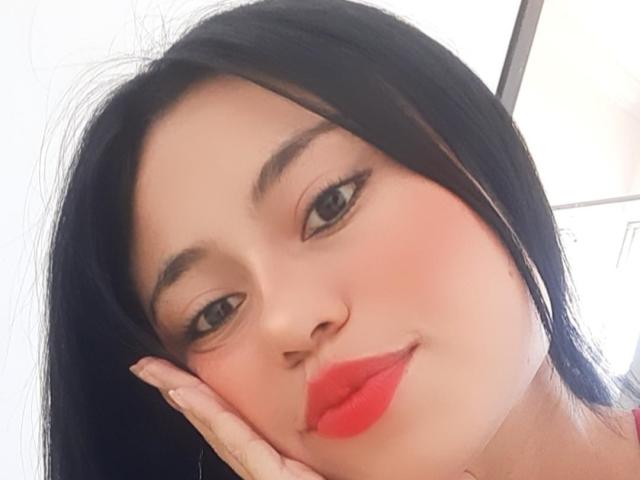 LolyFunX has black hair, red lips, and a cute smile with her hand on her cheek. She's looking at the camera with brown eyes and a slightly flushed face.