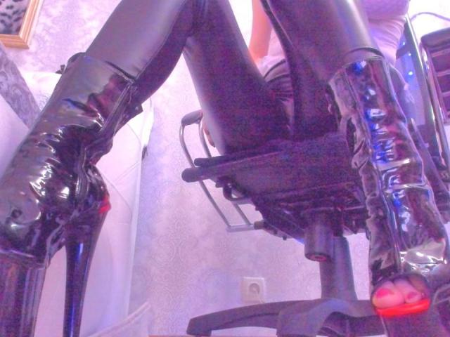 MiladyOne's shiny black latex boots with high heels are strapped to a chair, her black latex pants are tight around her ass, with a visible belt buckle in the middle.