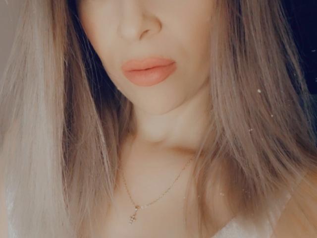 SophieDeee's face with pink lips, light brown shoulder-length hair, and a gold necklace with a small pendant. Her skin is fair, and her neck is visible.