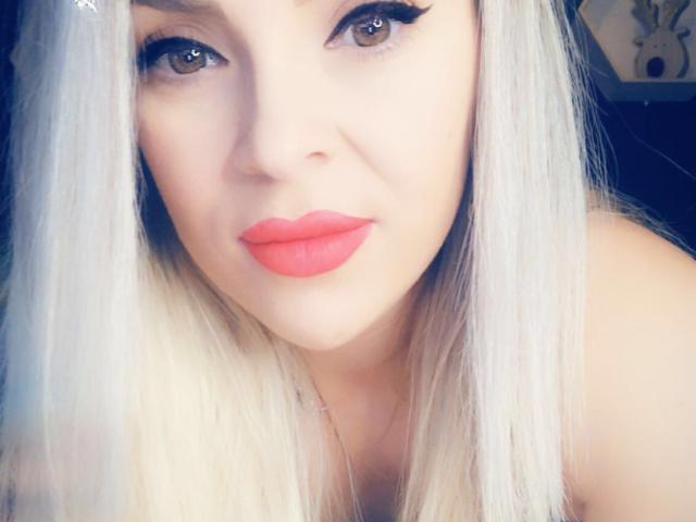 SophieDeee has pale skin, long white hair, and bright red lips. Her eyes are brown with black eyeliner, and she's looking directly at the camera with a slight smile.