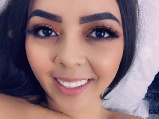 Il viso di EvaBrown, con un sorriso, sopracciglia scure, lunghe ciglia e rossetto rosa, ha occhi azzurri e capelli castani, appare carino e sensuale con la bocca leggermente aperta..