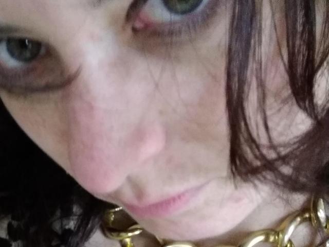 Il volto di LiveSex, con occhi verdi, naso rosa e un leggero rossore sulla guancia sinistra, con capelli castano scuro e una collana a catena dorata, in un selfie scattato con una leggera angolazione..