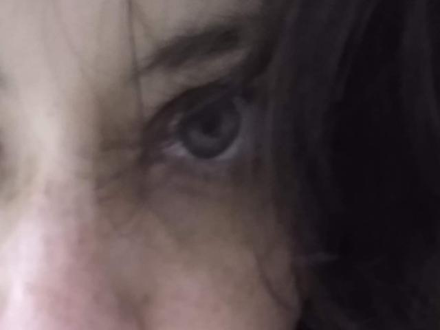 El ojo de LiveSex, de color marrón oscuro y ligeramente dilatado, es el centro de la fotografía borrosa, con el cabello oscuro y despeinado cubriendo parcialmente el lado izquierdo de su rostro..