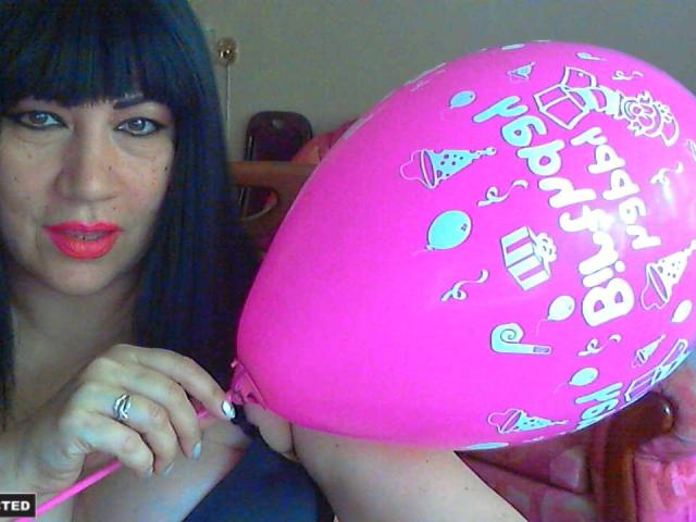 MelissaLight mit schwarzen Haaren, rotem Lippenstift und einem rosa Luftballon mit Partymotiven, der den Ballon mit ihrer rechten Hand hält und einen silbernen Ring zeigt. Der Ballon befindet sich in der Nähe ihrer Brüste..