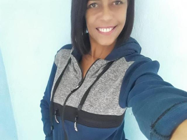 ErikaSpmt, avec une coupe de cheveux noire droite, souriante, portant un sweat à capuche bleu et gris avec fermeture éclair, prenant un selfie, montrant un visage mignon, de petites seins, et une expression détendue et heureuse..