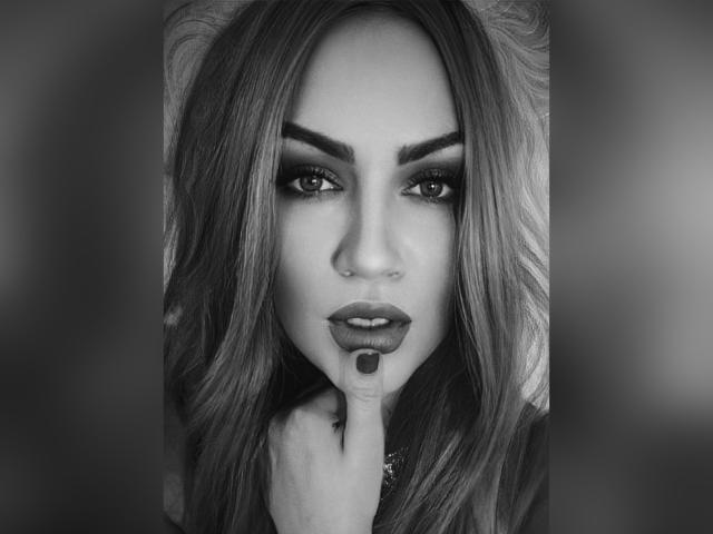 Fotografia in bianco e nero di SerafimaArt con capelli mossi, eyeliner scuro e labbra lucide. Sta toccando il labbro inferiore con un dito, guardando seducentemente la fotocamera..
