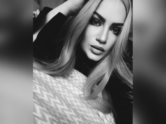 Zwart-wit foto van SerafimaArt met lang, steil, blond haar, donkere wenkbrauwen en volle lippen. Ze kijkt in de camera met een licht gekanteld hoofd..