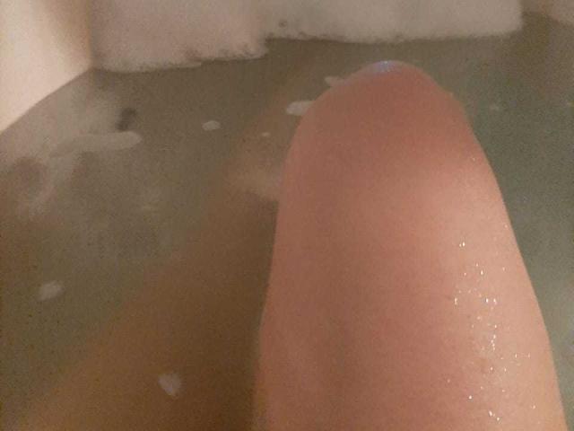 El pene erecto de Angelonix está en una bañera con agua de color verde, parcialmente sumergido, con burbujas alrededor de la base. La piel está húmeda, mostrando un ligero tono rosado en la punta..