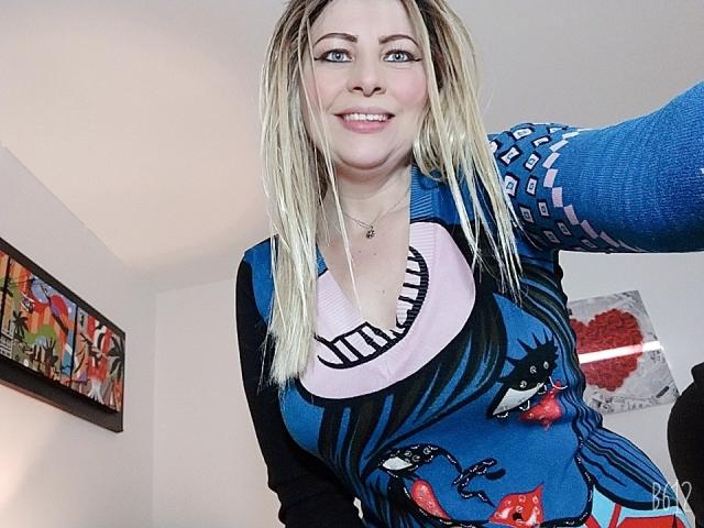SaraSupreme a les cheveux blonds, porte une robe noire et bleue à motifs, a de grandes seins, sourit et porte un collier. Elle prend un selfie, exhibant ses seins et ses fesses..
