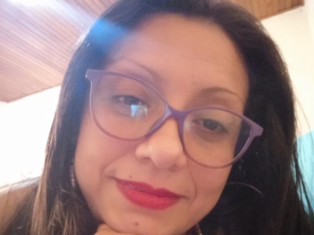 La signorina Sara, con gli occhiali viola, i capelli castano scuro, il rossetto rosso, un leggero sorriso e una piccola lentiggine sotto l'occhio destro. Il suo naso è leggermente all'insù..