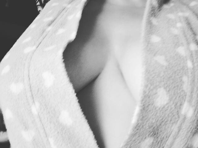 La grande robe moelleuse et à pois de Mistress Sara est ouverte, révélant ses seins volumineux, doux et légèrement arrondis. L'image en noir et blanc met en valeur sa poitrine et la texture de sa robe..