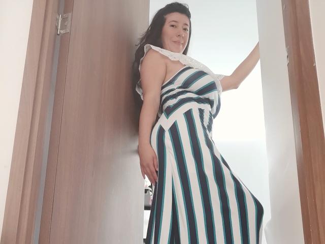 HotPamelaSex in a striped dress, standing in a doorway, her ass slightly visible, smiling, with one hand on the door, her tits subtly outlined, long dark hair.