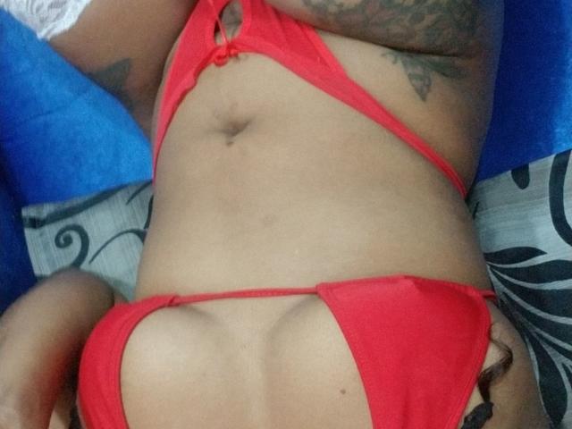 KathHott's red bikini with cut-out sides, showing her tan skin and tattoos, and her small, perky tits. Her flat, toned stomach is visible. She's lying down.