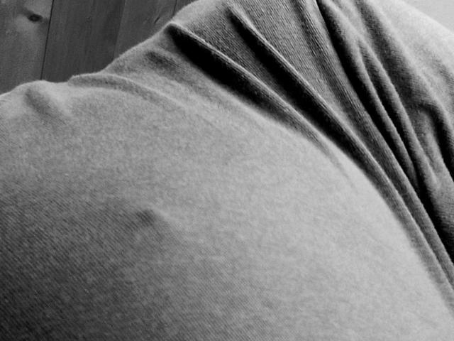 Akinoukk's gray, slightly wrinkled, and textured shirt covers their ass, with a small dark spot visible on the left side. Black and white, close-up, slightly tilted.