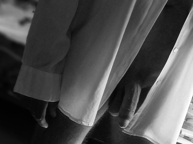 Akinoukk's ass in loose, dark-colored pants reflected in a mirror. Their flaccid, uncircumcised penis is visible beneath the pants, slightly hanging. Black-and-white photo, mirror reflection.
