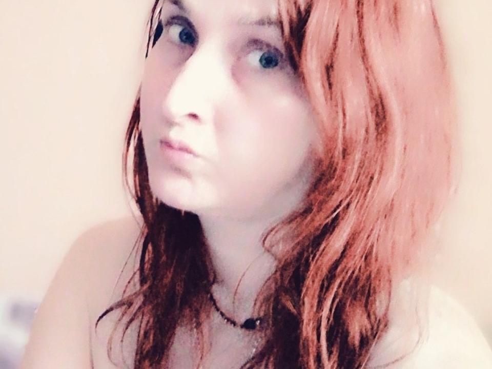 MssAngela tiene la piel pálida, el cabello rojo y brillante, y una expresión seria. Lleva un collar negro y tiene los pechos parcialmente visibles. Sus ojos son azules..