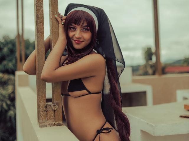 SerenaDeStark con cabello rojo largo, vestida con un hábito de monja, usando un bikini negro, mostrando pequeños senos, de pie contra un pilar de madera, sonriendo con lápiz labial rojo..