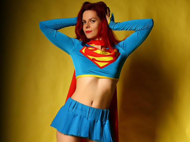 MelanyTessk with red hair, wearing a blue Supergirl outfit, exposing her midriff, hands in her hair, yellow background, skirt up, showing her ass, confident smile.