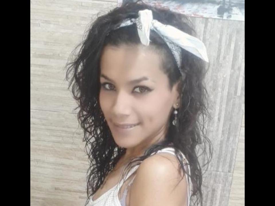 Moonka69, con i capelli neri ricci e umidi, una fascia bianca e degli orecchini, sorride alla fotocamera, mostrando il suo viso carino e i suoi piccoli seni, indossando una canotta bianca..