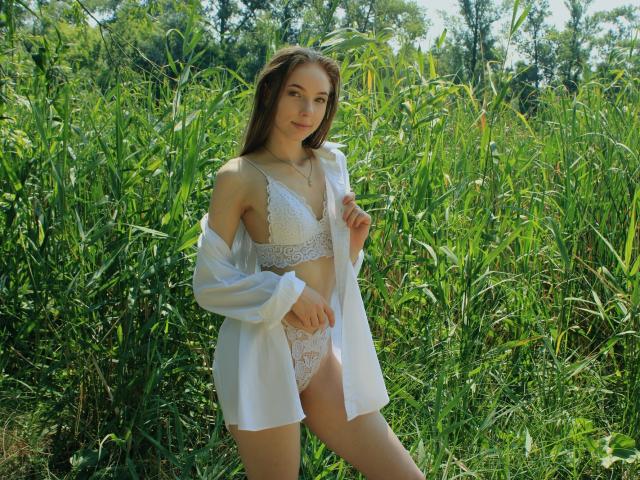 SafiraFuracao staat in een groen veld, gekleed in witte kant lingerie en een open shirt, met lang bruin haar en een zelfverzekerde glimlach, waarbij ze haar kleine borsten en schattige vulva laat zien..