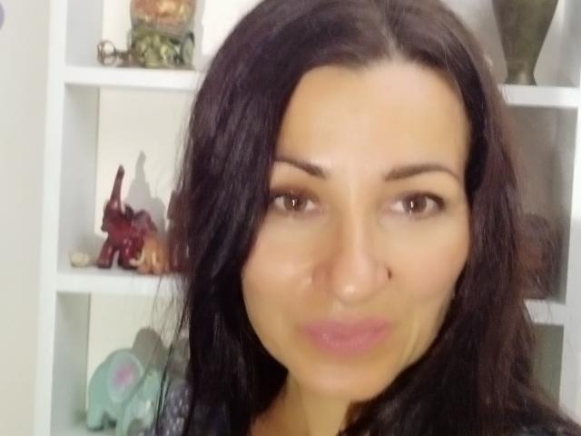 GinaONeon has dark brown eyes, long black hair, and is puckering her lips in a selfie with a cute nose. Her tits aren't visible. She's in a room.