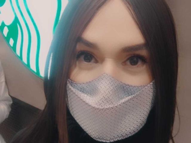 Jhovanna, mit braunen Haaren, trägt eine gewebte Gesichtsmaske, die Nase und Mund bedeckt. Ihre braunen Augen schauen in die Kamera. Ihre Maske ist grau und hat eine gewebte Textur..