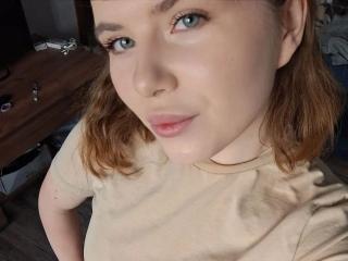 AlysiaFillingham has blue eyes, light skin, and brown hair. She's wearing a beige shirt, looking up with a slight smile, and has a small nose piercing.