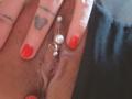 FrenchShanna's pinkish-brown pussy with a silver clitoral piercing, featuring three small balls. Her red-painted nails rest on her skin, showing a tattoo of a heart and lines.