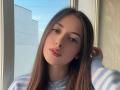 BokSinha has long brown hair, blue eyes, and is wearing a blue and white striped sweater. Her pink lips are slightly parted, and she's gazing to the side.