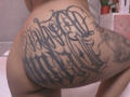 GabyMathew's ass has a large, intricate black tattoo covering the right buttock and upper thigh, featuring bold, cursive lettering. Her skin is light brown.