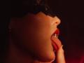 JaneWow's face in profile, tongue out with a silver ring, red lips, black lace mask, hand touching chin, dark red light highlighting her skin.