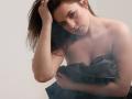 Dreia with dark brown hair, looking down, has her hand in her hair, covering her tits with a black, slightly ripped cloth, showing a sad or tired expression.