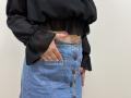 Tilliana's hand with pink nails in a denim skirt's pocket, black sheer blouse, and exposed midriff. Skirt has brown buttons, black blouse has puffed sleeves.