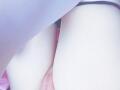 As coxas pálidas de Gracie estão abertas, revelando sua vulva rosa com uma tanga preta puxada para o lado, sob um tecido branco, ligeiramente transparente..