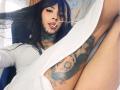 AnneKisss with black hair, tattoos on neck and arm, white shirt, sucking on a straw, showing her tits and pussy, her arm over her ass.