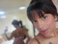 TeylorJenkins with glasses, brown lace bra, large tits, looking down, hand near mouth, subtle smile, dark hair, light skin, indoors, low angle, soft lighting.