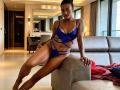 RoldanStefy with dark skin, tattoos, and black hair in a bun, wearing blue lace lingerie with strappy details, sitting on a grey couch, legs spread, showing her ass.