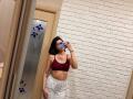 HeikeCarchi with medium tits in a red bra, white brick wall, holding phone, gray sweatpants, black hair, tattoo on right arm, standing in front of a mirror.