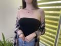 Nesie has a strapless black top, pink and black plaid shirt off her shoulders, blue jeans, and a necklace, with her hands near her crotch.